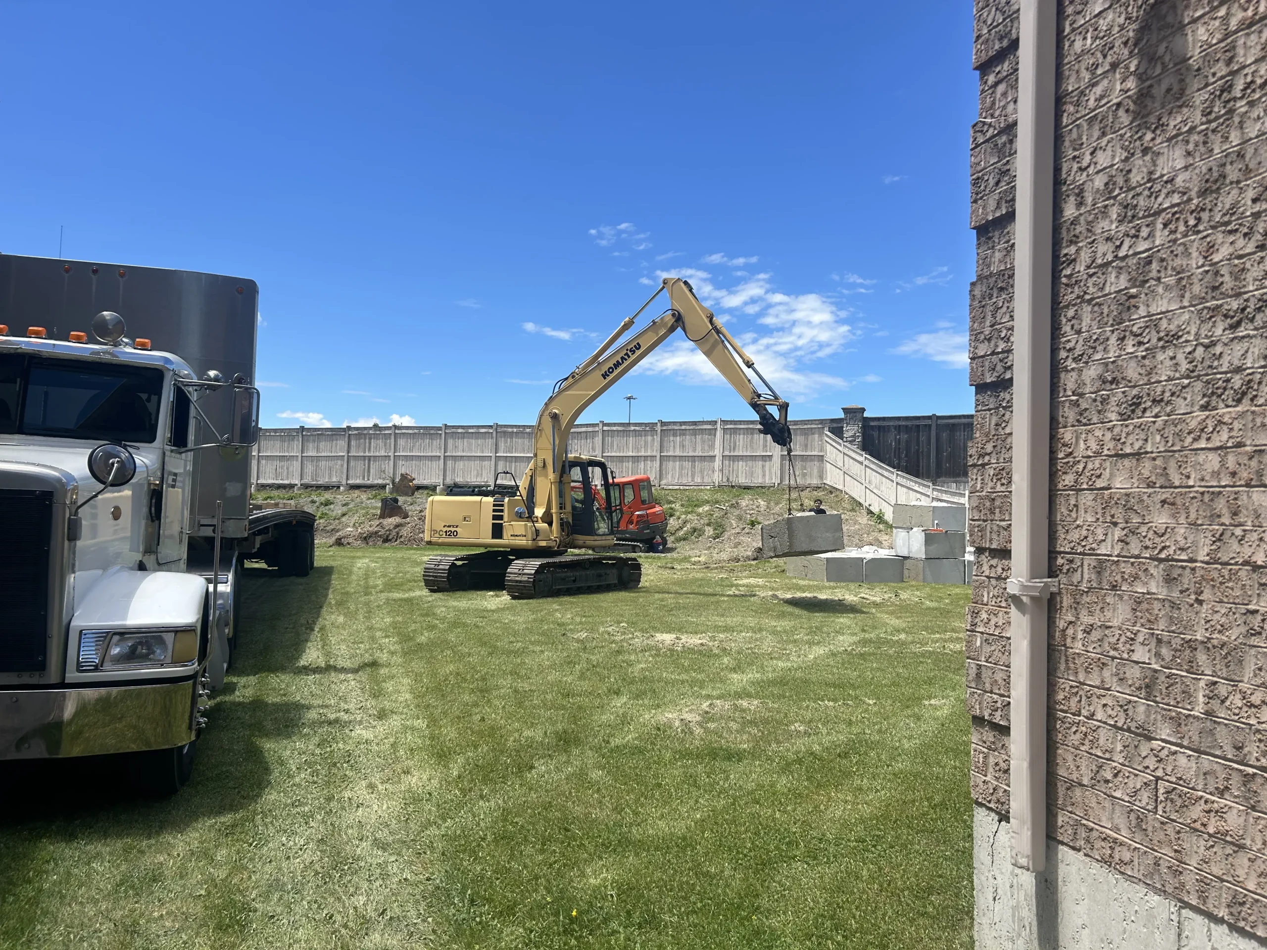 Excavator placing precast retaining wall blocks during a retaining wall installation project in Richmond Hill, Ontario by RHGroundwork.
