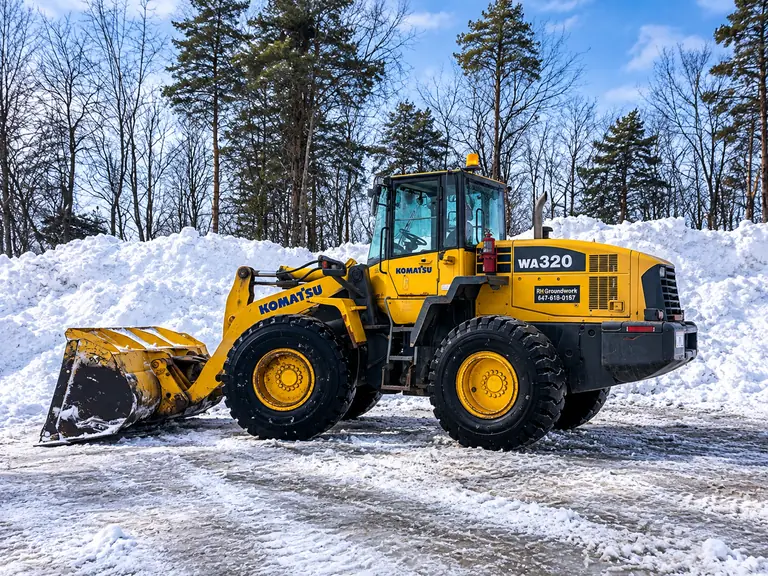 RH GroundWork Komatsu WA320 wheel loader parked beside a snowbank, equipped for commercial snow removal.
